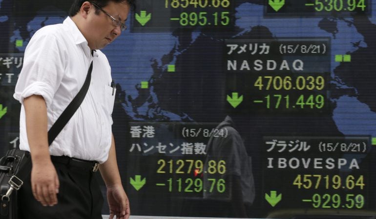 Un empresario pasa delante de una pantalla que muestra información bursátil en Tokio, bolsa que se desplomó este lunes casi 900 puntos.