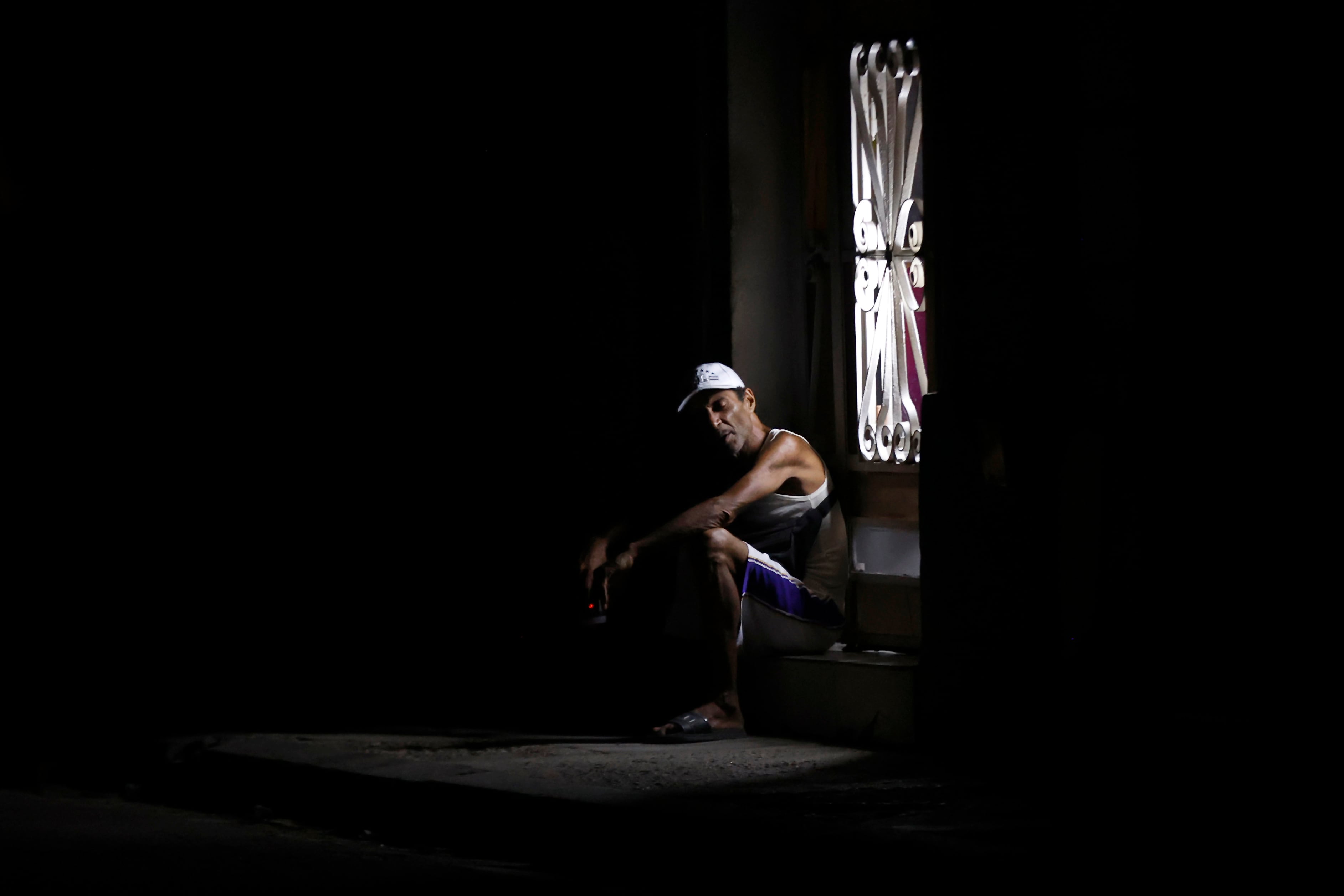 AME032. LA HABANA (CUBA), 01/07/2025.- Fotografía de una persona sentada en la puerta de su casa durante un apagón este lunes, en La Habana (Cuba). El 45 % de Cuba estará afectada de forma simultánea por apagones en el horario de mayor demanda de energía en la tarde-noche este martes, acorde con los cálculos de la empresa estatal Unión Eléctrica (UNE), que advierte de cortes durante todo el día. EFE/ Ernesto Mastrascusa