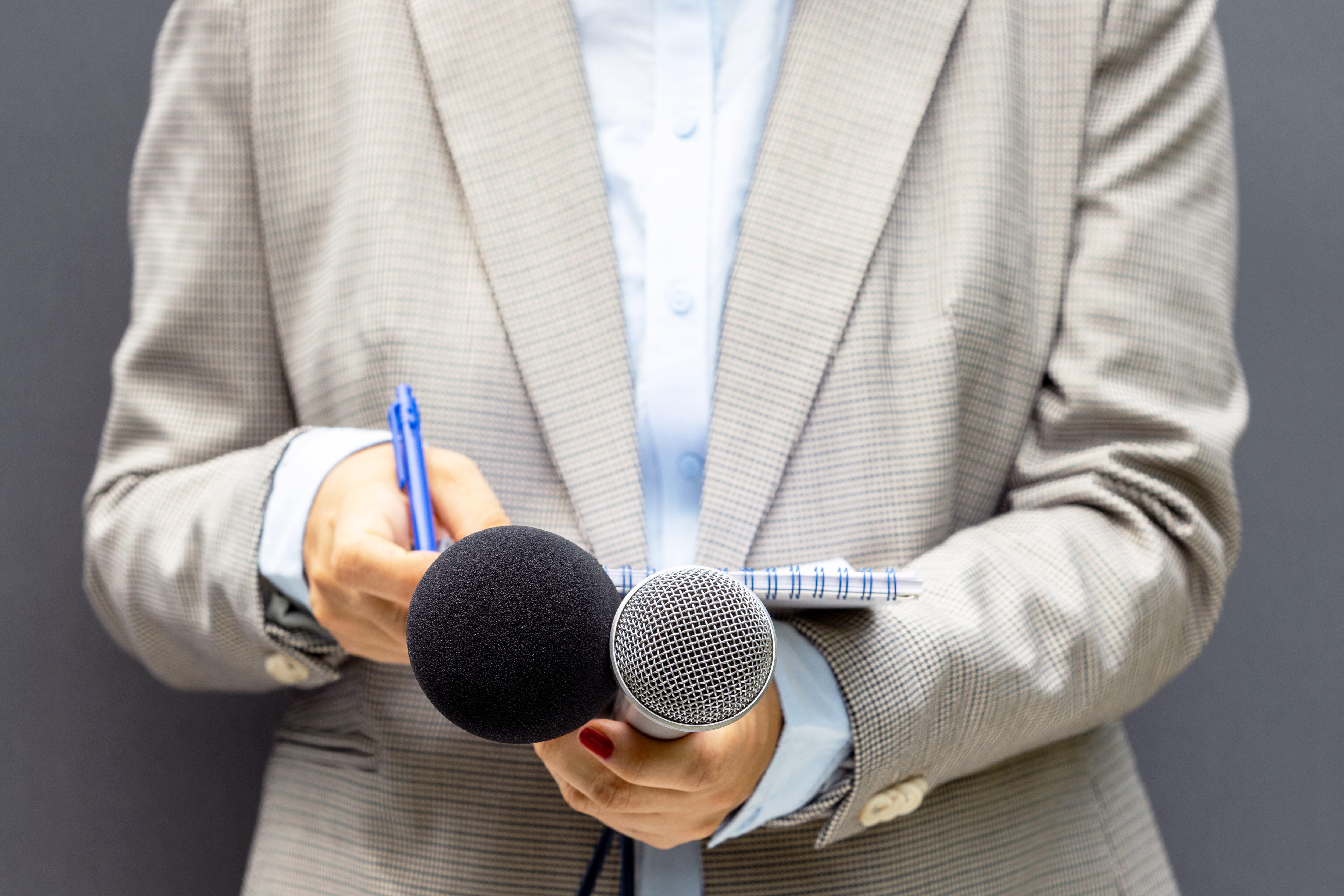Female journalist at news conference or media event, writing notes, holding microphone