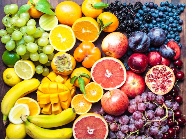 Diferentes tipos de frutas enteras y cortadas sobre una mesa (Getty Images)