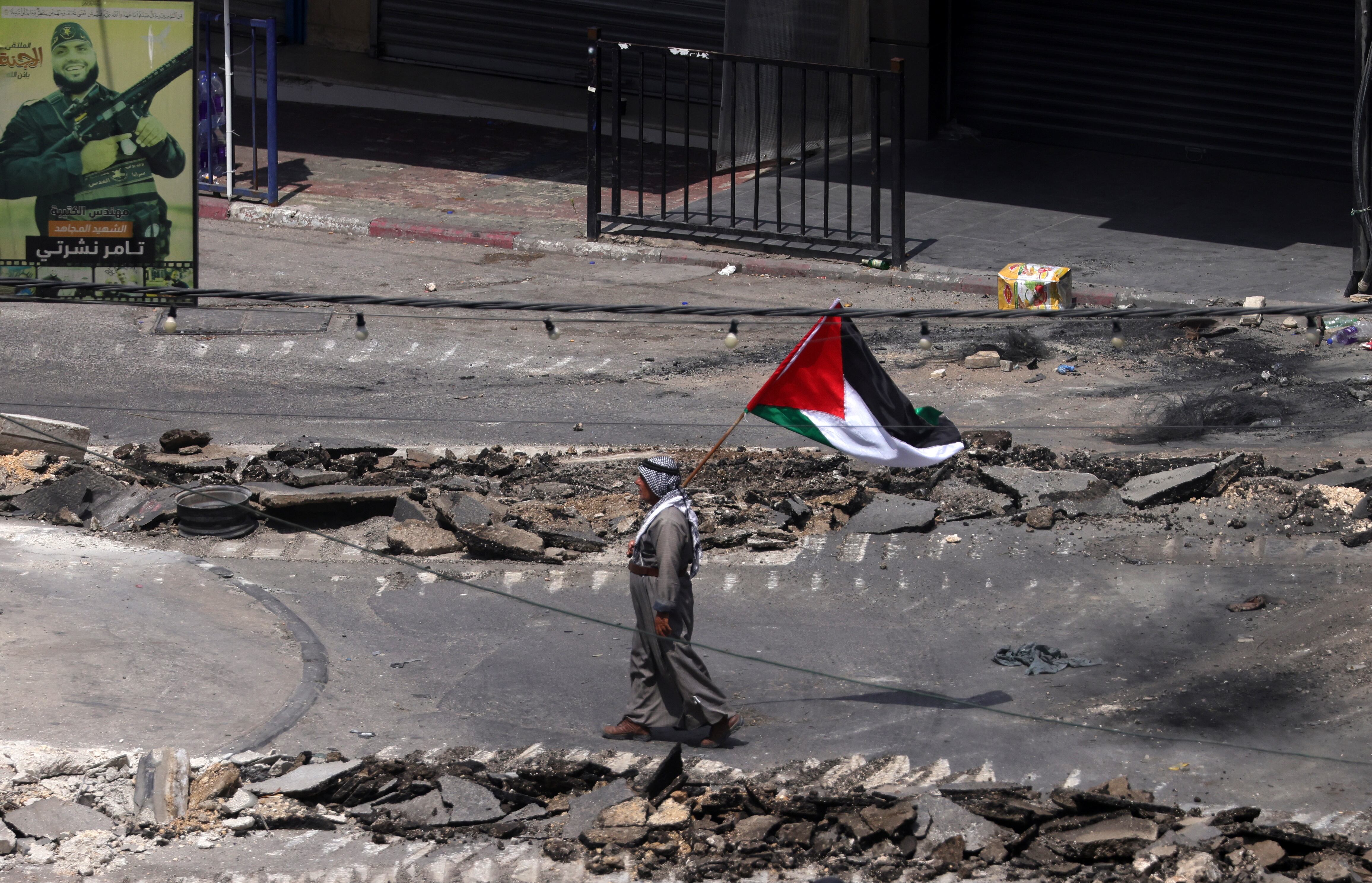 Un palestino ondea una bandera palestina mientras camina por una calle dañada durante el sexto día de una operación militar israelí en la ciudad cisjordana de Yenín.
EFE/ Alaa Badarneh
