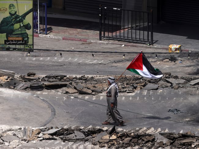 Un palestino ondea una bandera palestina mientras camina por una calle dañada durante el sexto día de una operación militar israelí en la ciudad cisjordana de Yenín.
EFE/ Alaa Badarneh
