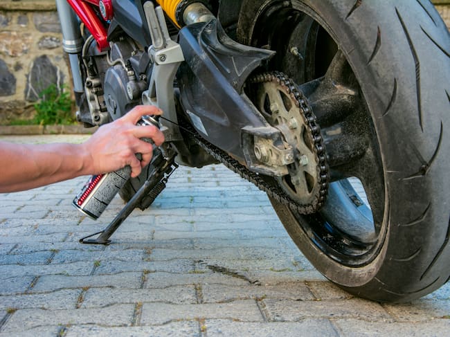 Persona lubricando la cadena de una moto (Foto vía GettyImages)