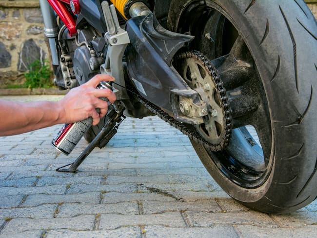 Persona lubricando la cadena de una moto (Foto vía GettyImages)