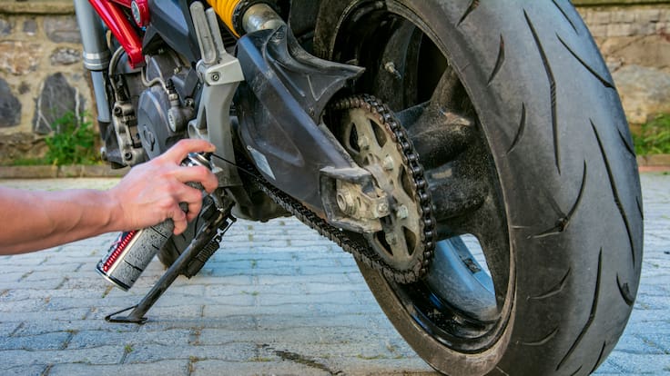 Persona lubricando la cadena de una moto (Foto vía GettyImages)