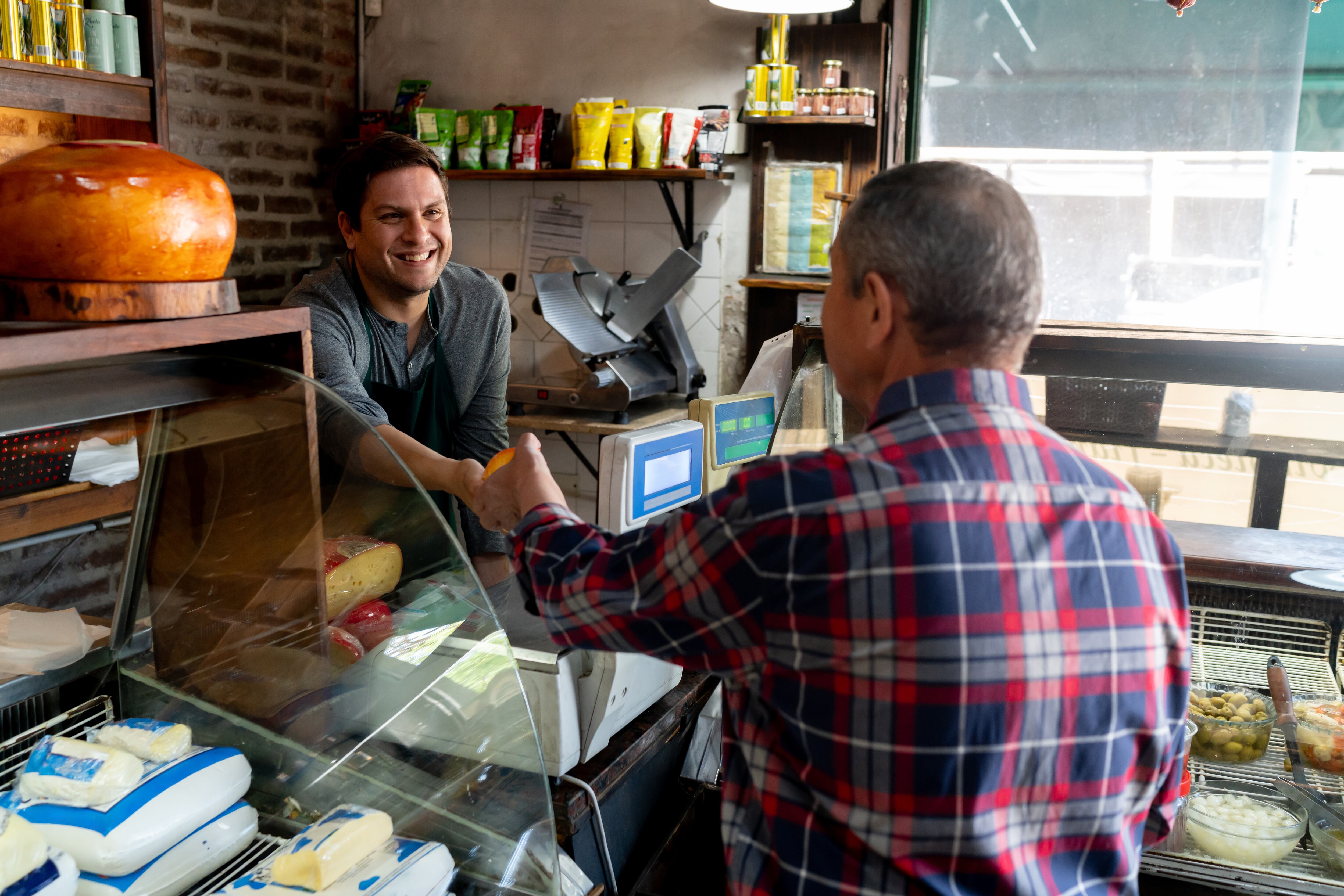 Friendly salesman handing block of cheese to unrecognizable senior customer at the deli - People at work concepts and consumerism concepts
