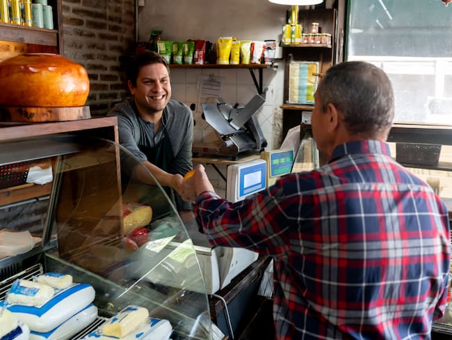 Friendly salesman handing block of cheese to unrecognizable senior customer at the deli - People at work concepts and consumerism concepts