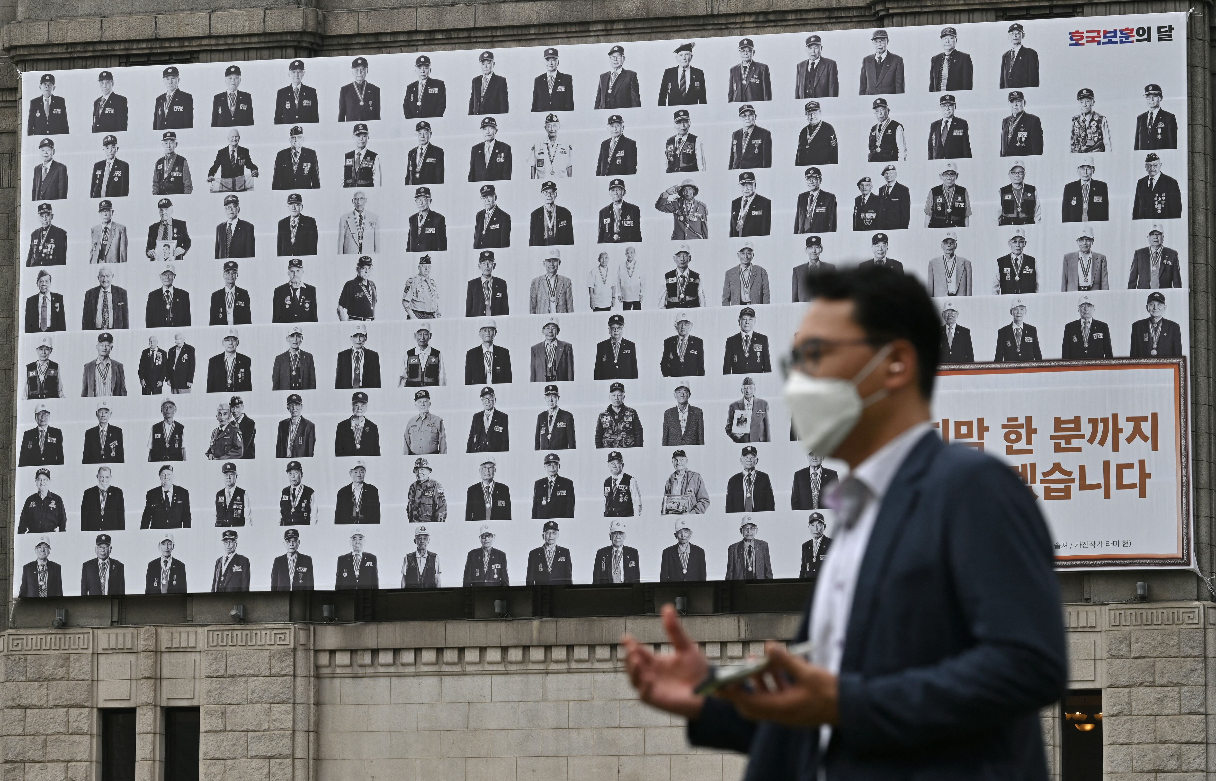 A man walks past a banner showing portraits of Korean War veterans hanging in front of City Hall in Seoul on June 25, 2021, on the 71st anniversary of the outbreak of the Korean War. (Photo by Jung Yeon-je / AFP) (Photo by JUNG YEON-JE/AFP via Getty Images)