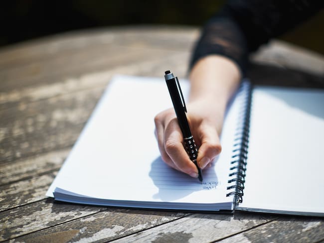Mujer escribiendo en un cuaderno con un esfero o lapicero de tinta negra / Foto: GettyImages
