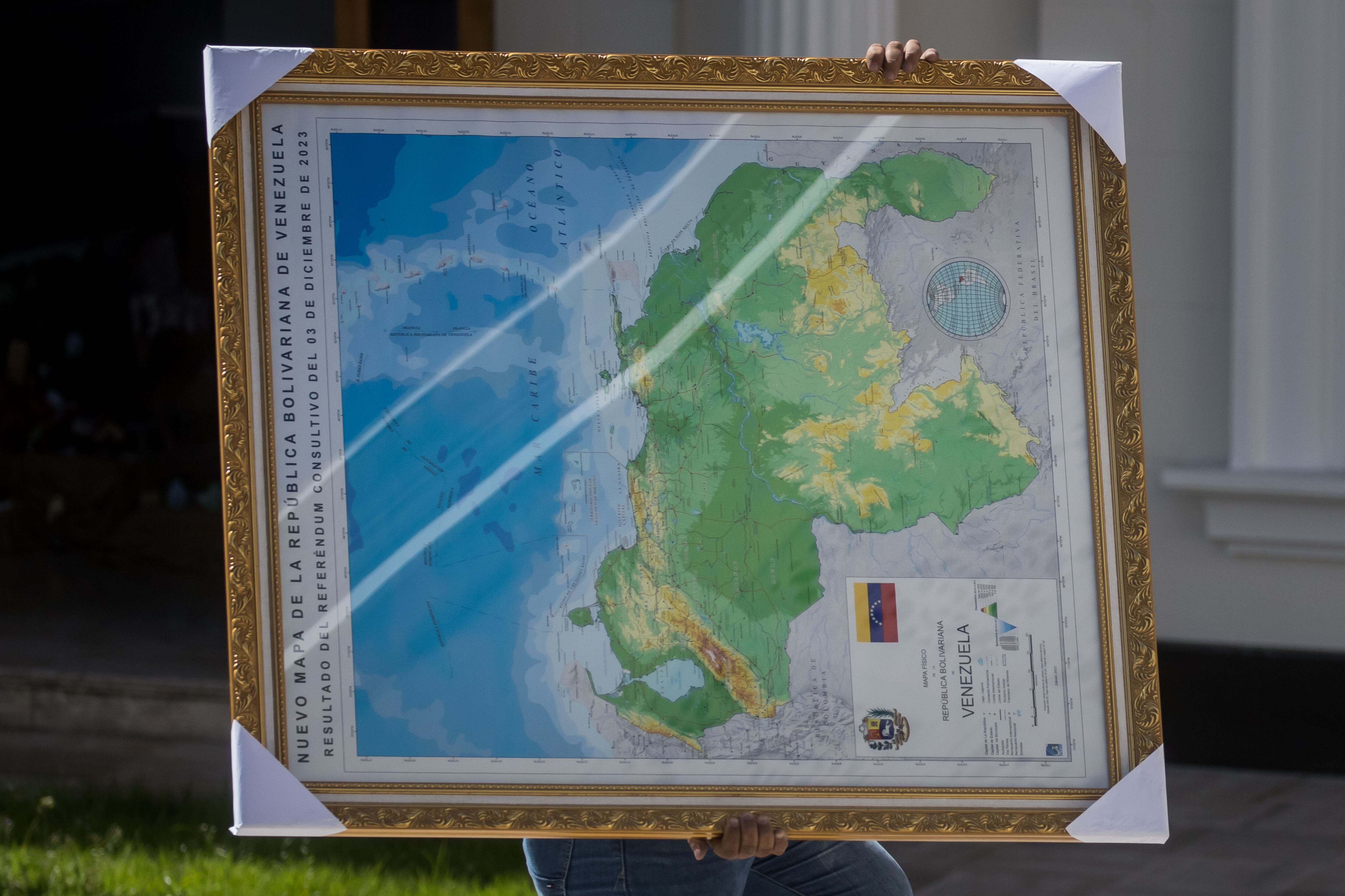 AME2481. CARACAS (VENEZUELA), 06/12/2023.- Un hombre carga hoy un cuadro del mapa de Venezuela con la adhesión del Esequibo, en uno de los jardines del Palacio Federal Legislativo en Caracas (Venezuela). La Asamblea Nacional (AN, Parlamento) de Venezuela, controlada por el chavismo, prevé aprobar dentro de una semana la ley de anexión del territorio en disputa con Guyana, en cumplimiento del referendo unilateral celebrado el domingo relacionado con este conflicto, aseguró el presidente de la Cámara, Jorge Rodríguez. EFE/ MIGUEL GUTIERREZ