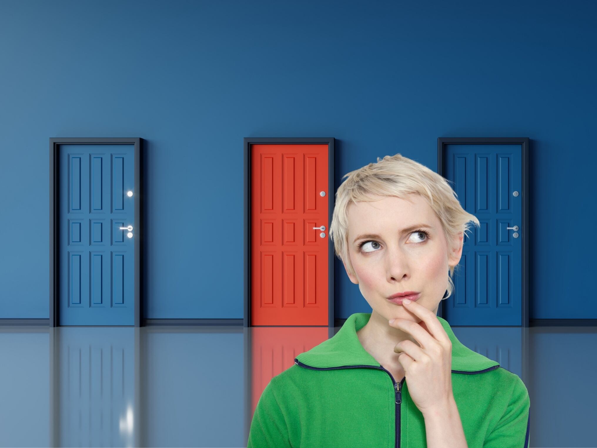De fondo: Tres puertas alineadas. Dos de ellas son azules y la del medio es roja, rompiendo con el tono uniforme. Al frente hay una mujer haciendo gestos de duda (Crédito: Getty Images)