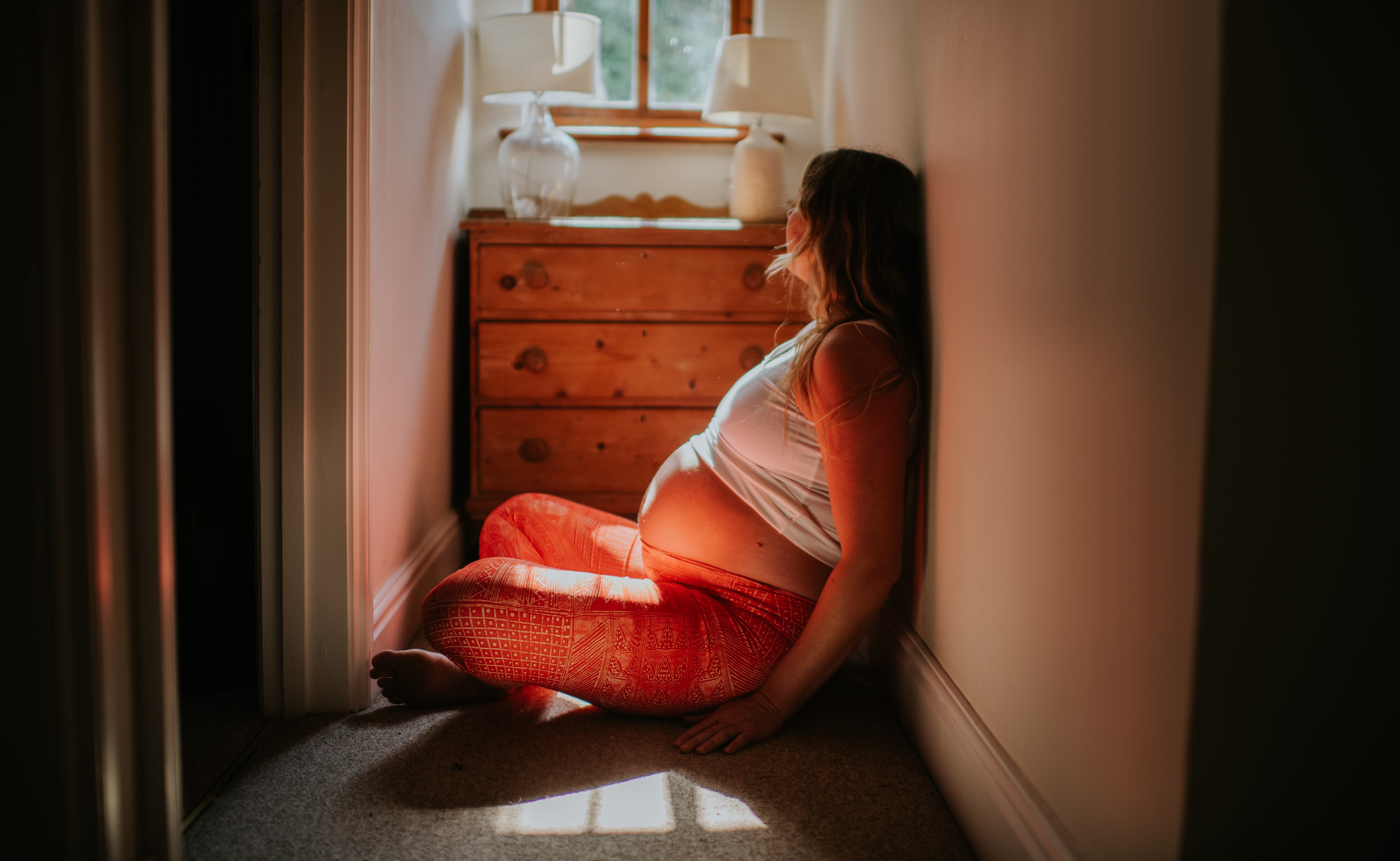 En portada: Mujer embarazada, sentada en un pasillo que lleva a su cuarto mientras mira meditabunda a la ventana que lleva al exterior (Crédito Getty Images)