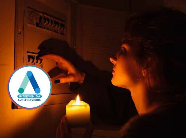 Persona sin luz con vela en la mano, mirando interruptores de la energía. Al lado, logo de la empresa Air-E intervenida. 