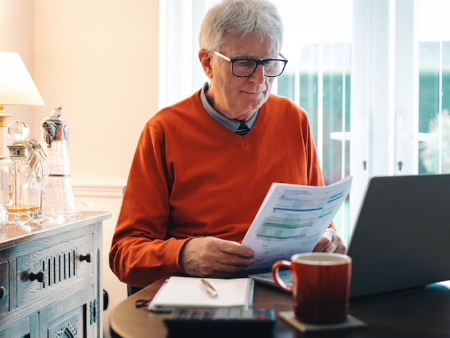 Hombre mayor revisando papeles en su comedor (Getty Images)