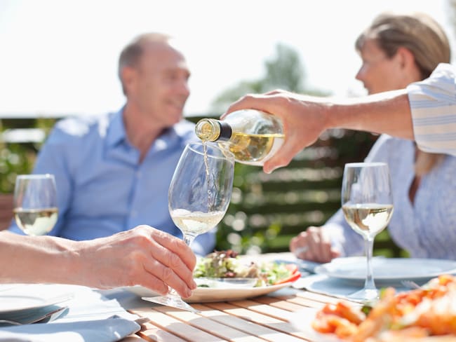 Hombre sirviendo vino en una copa, mientras se disfruta de una cena familiar al aire libre (Getty Images)