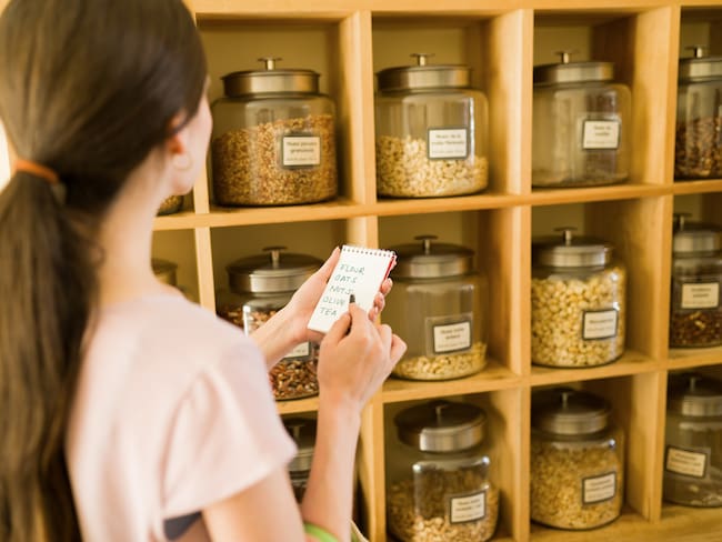 Mujer revisando una lista de compras, mientras observa una repisa con varios cereales (Getty images)