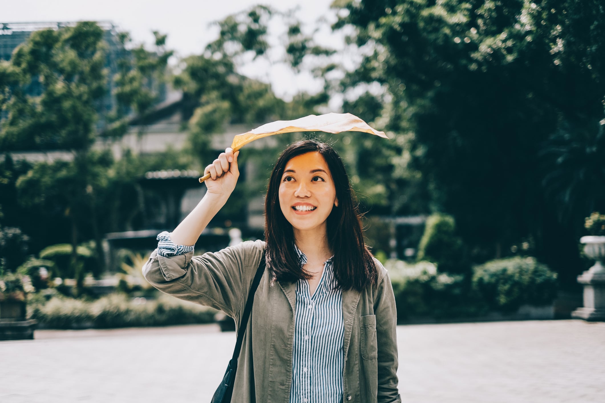 Mujer alegre y sonriente protegiéndose con una hoja caída bajo el sol en el parque. Foto: Getty Images.