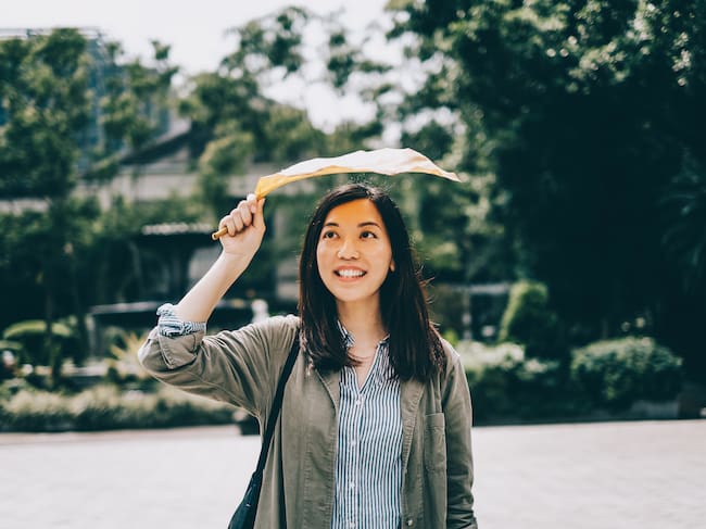 Mujer alegre y sonriente protegiéndose con una hoja caída bajo el sol en el parque. Foto: Getty Images.