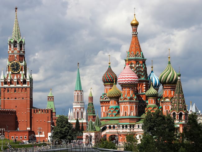 Moscow - July 2019: looking at the famous colorful domes of the Saint Basil's Cathedral and the Spasskaya Tower of the Kremlin, with sun in the front and clouds approaching in the back