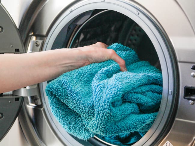 Persona introduciendo una toalla azul en la lavadora. (Foto vía Getty Images)