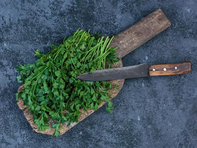 Ramo de cilantro sobre una tabla de madera de cortar con un cuchillo (Getty Images)