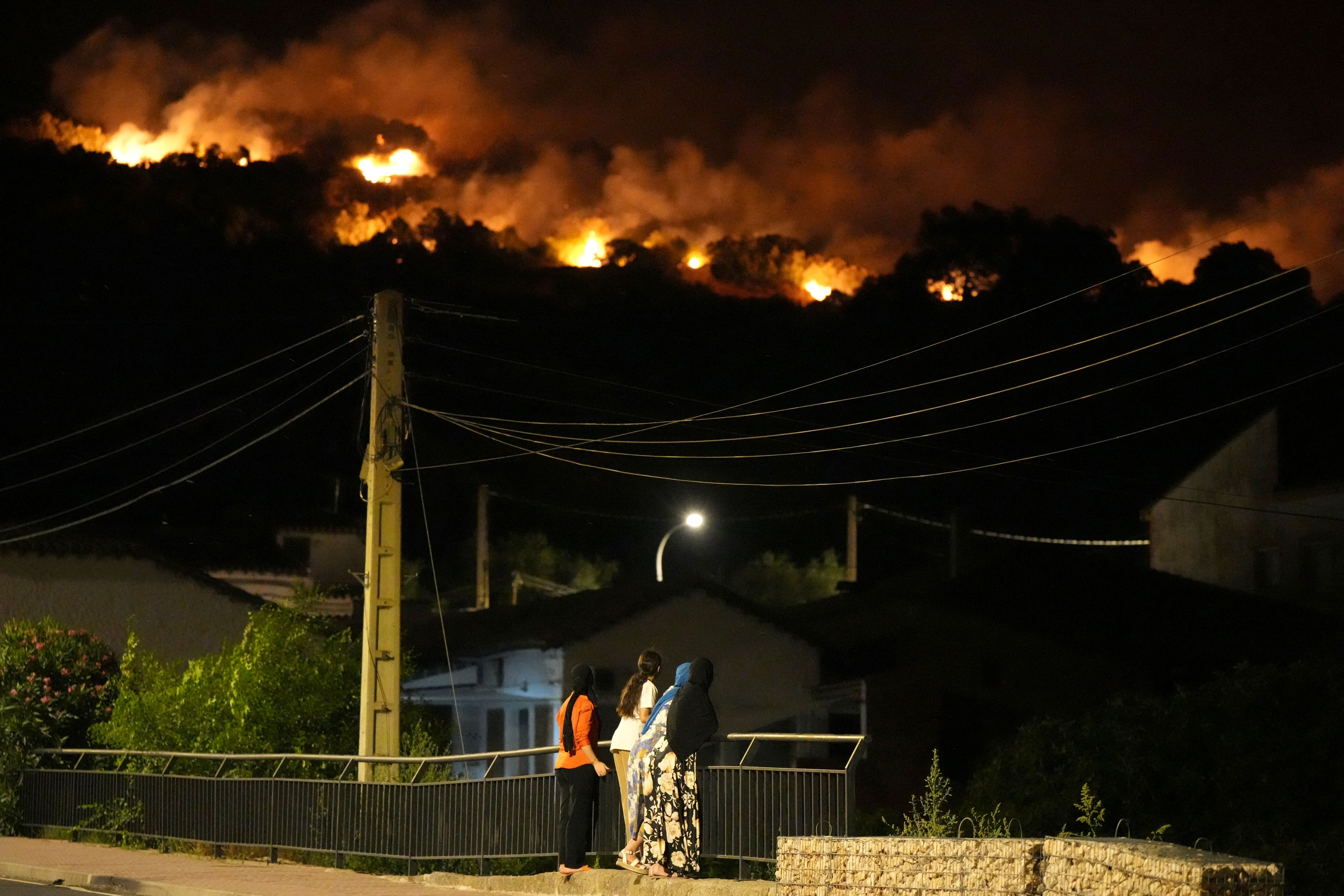 Los residentes observan las llamas en las cimas de las colinas mientras los bomberos combaten un incendio forestal en la zona de Cebreros, cerca de Ávila, a 80 km al oeste de Madrid, la noche del 24 de julio de 2026. Los peores incendios forestales de la historia de la Comunidad de Madrid asolan el oeste de la capital española, obligando a las autoridades a evacuar o a ordenar a unas 40.000 personas que permanezcan en sus casas. (Foto de César Manso / AFP)