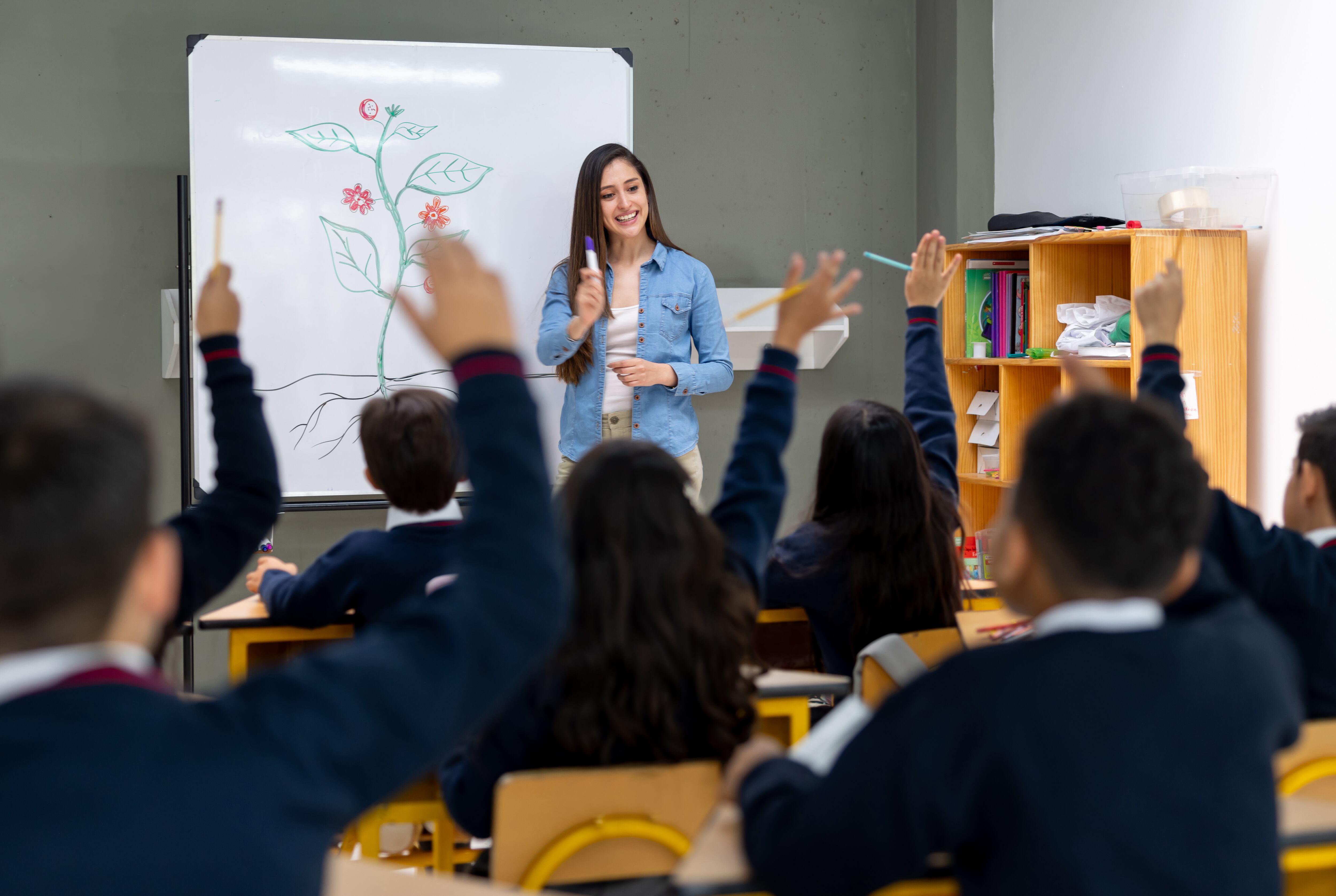 Latin American students raising their hand after the teacher asked a question in class at an elementary school