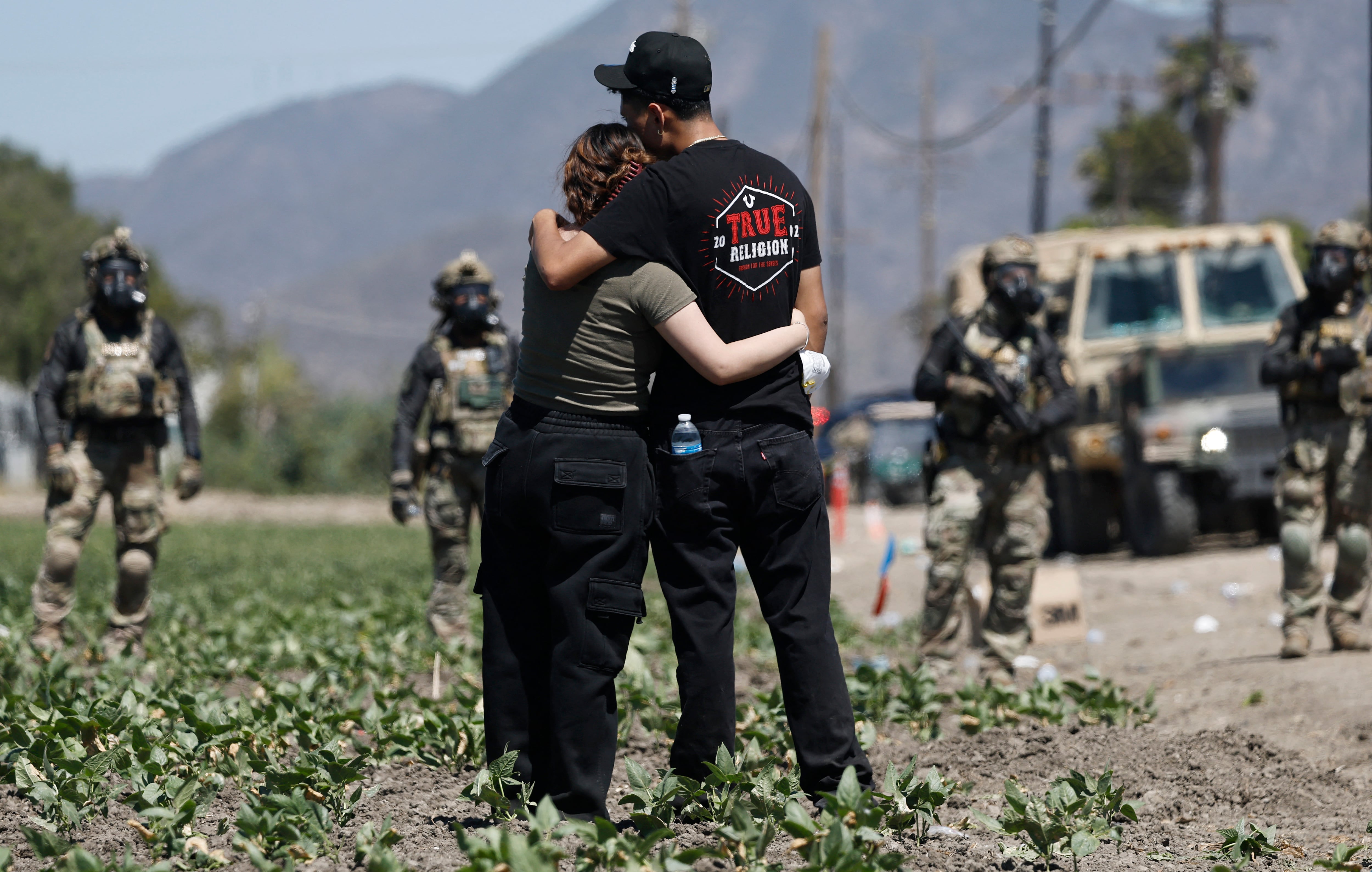 CAMARILLO, CALIFORNIA - JULY 10: People embrace near federal agents blocking a road during an ICE immigration raid at a nearby licensed cannabis farm on July 10, 2025 near Camarillo, California. Protestors stood off with federal agents for hours outside the farm in the farmworker community in Ventura County. A Los Angeles federal judge is set to rule Friday on a temporary restraining order which would restrict area immigration enforcement operations.   Mario Tama/Getty Images/AFP (Photo by MARIO TAMA / GETTY IMAGES NORTH AMERICA / Getty Images via AFP)