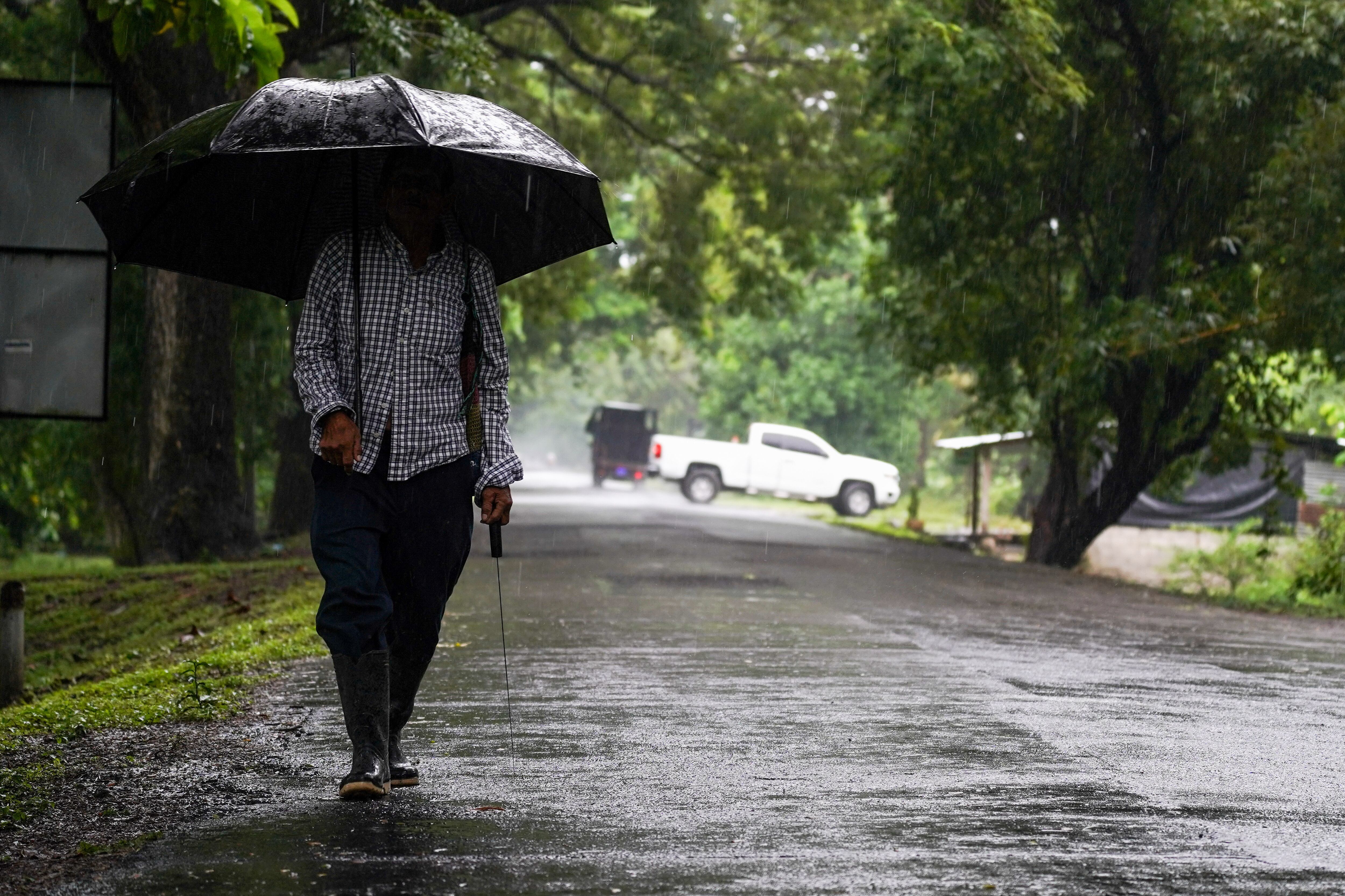 SAN NICOL·S LEMPA, EL SALVADOR - 2023/10/31: A man shelters from the rain while walking home. El Salvadoran government released a national state of emergency due to Storm Pilar. According to the US National Hurricane Center, Storm Pilar brought heavy rains to EL Salvador. They informed the public that heavy rains would produce flash and urban flooding and mudslides in higher terrain areas. (Photo by Camilo Freedman/SOPA Images/LightRocket via Getty Images)