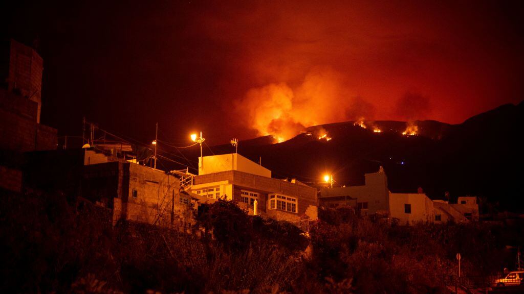 A picture taken in the night of August 19, 2023 shows the fronts of the forest fire on hills above houses, in the Guimar valley on the Canary Island of Tenerife. The blaze, which officials say is the most "complex fire" to hit the Canary Islands in 40 years, broke out on August 15 in a mountainous area of northeastern Tenerife. 225 firefighters are struggling against the ferocious blaze which has so far destroyed nearly 5,000 hectares (more than 12,000 acres) of land, has a perimeter of 50 kilometres (30 miles) and led to the evacuation and/or confinement of some 7,600 people from nine population centers. (Photo by DESIREE MARTIN / AFP) (Photo by DESIREE MARTIN/AFP via Getty Images)