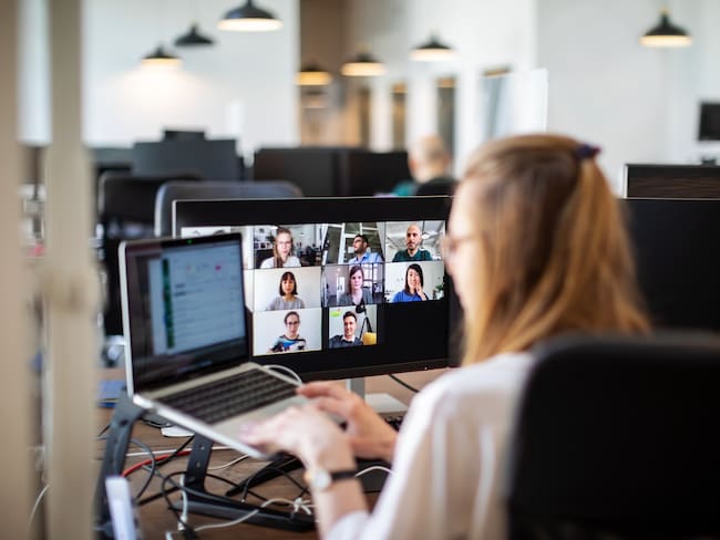 Businesswoman working on her laptop and having a video conference at her work desk. Rear view of a woman discussing work on video call with team members. Back to work post corona virus pandemic lockdown.