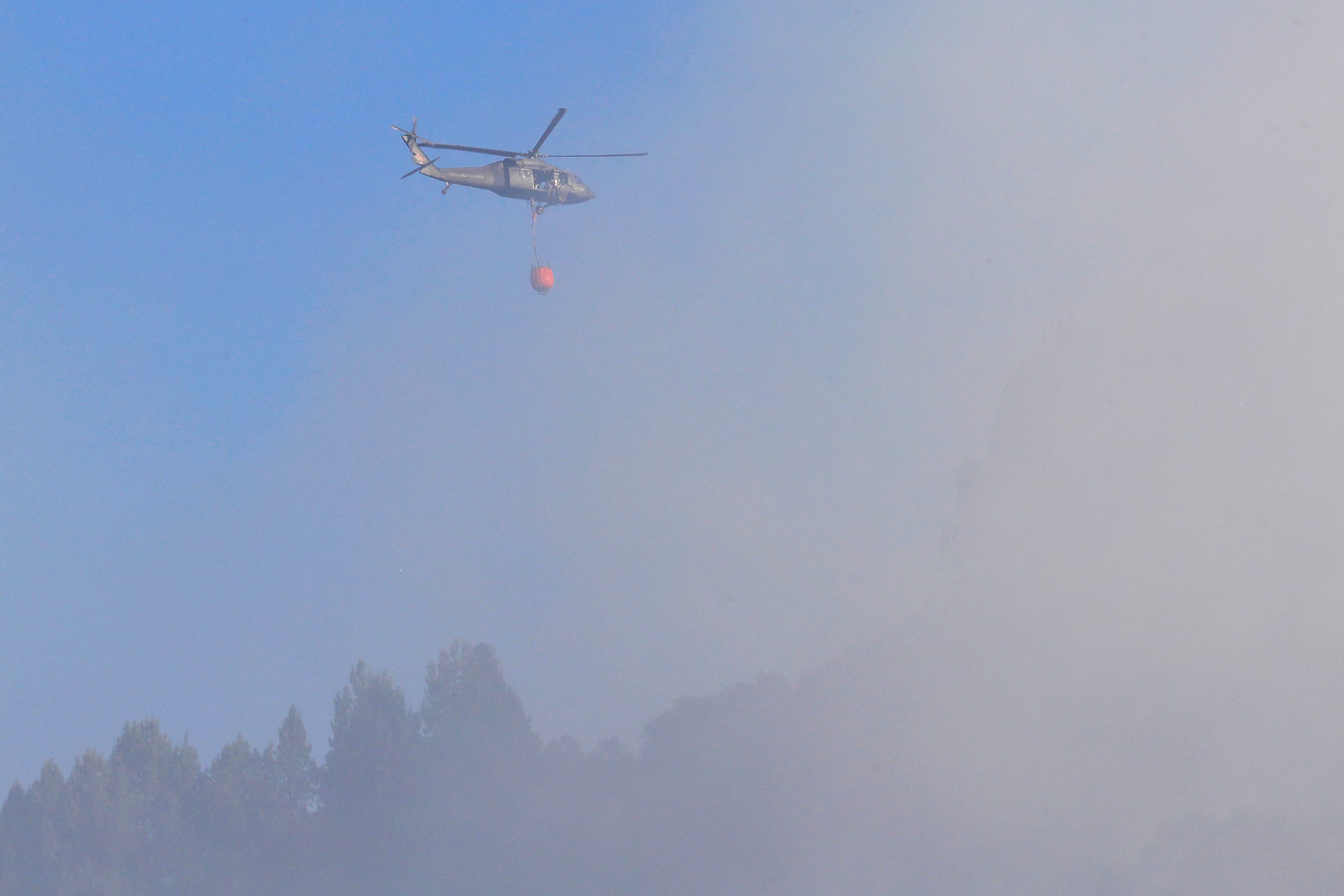 BOG400. BOGOTÁ (COLOMBIA), 22/01/2024.- Un helicóptero, que utiliza el sistema Bambi bucket, arroja agua entre el humo que se observa hoy en los cerros orientales en Bogotá (Colombia). Bomberos, la Defensa Civil y las fuerzas de seguridad trabajan desde la mañana de este lunes para extinguir un incendio en los cerros de Bogotá que ha llenado de humo el oriente de la capital colombiana. EFE/ Carlos Ortega