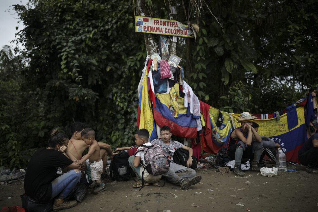Migrantes sentados bajo un cartel que marca la frontera entre Panamá y Colombia durante su viaje a través del Tapón del Darién, el 9 de mayo de 2023. (Iván Valencia / Foto AP)