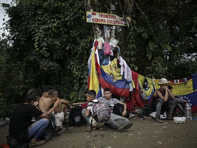 Migrantes sentados bajo un cartel que marca la frontera entre Panamá y Colombia durante su viaje a través del Tapón del Darién, el 9 de mayo de 2023. (Iván Valencia / Foto AP)