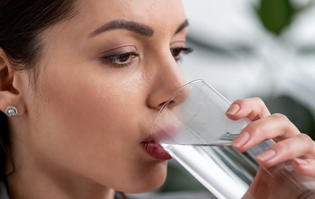 portrait of beautiful businesswoman with sweaty face drinking water from glass while suffering from heat