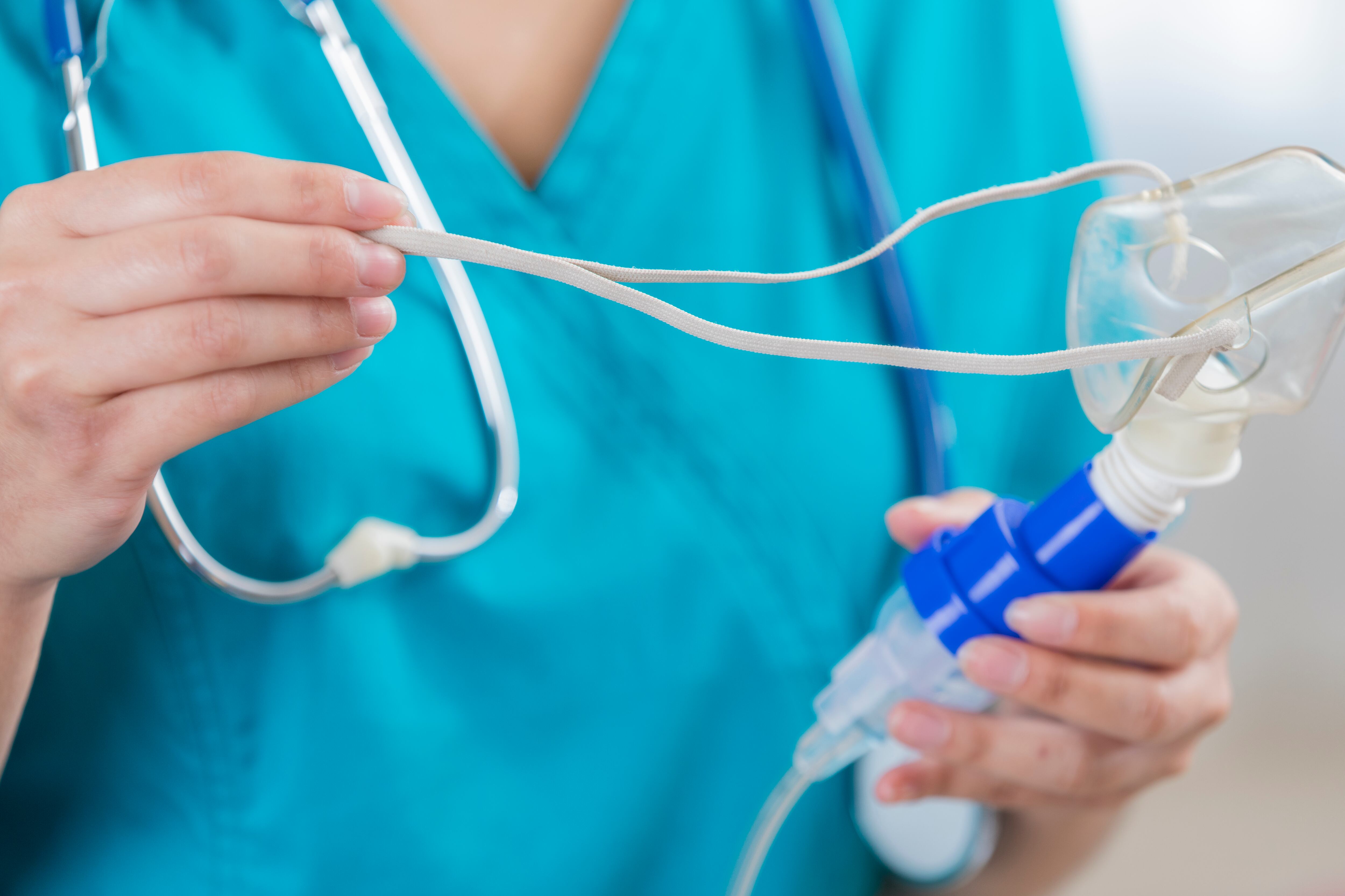 Unrecognizable female nurse holds a pediatric nebulizer. The nurse is wearing scrubs and a stethoscope.