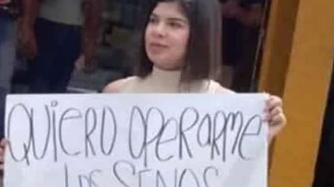Una mujer que sostiene un aviso con un polémico mensaje que dice "quiero operarme los senos, ¿me ayudas?",