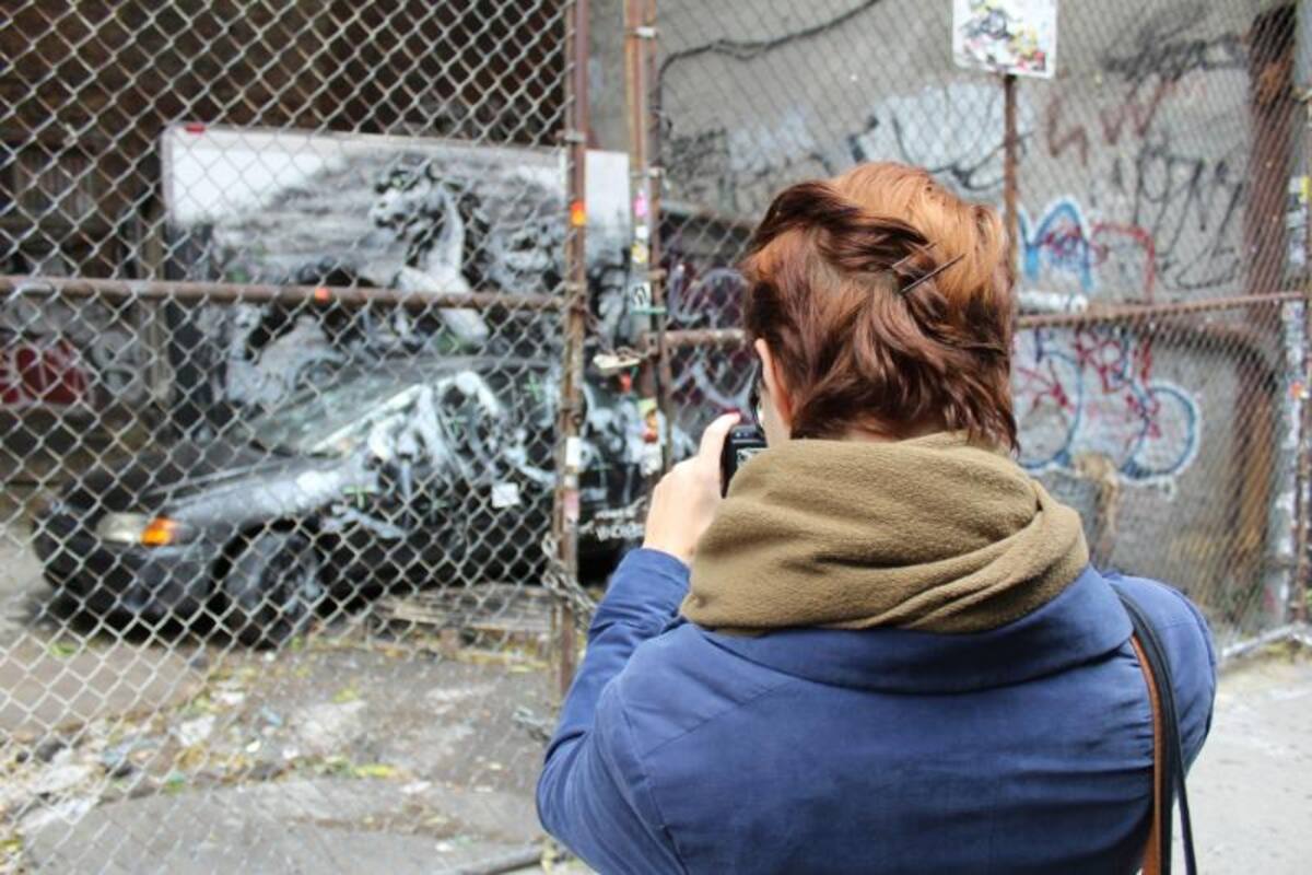 Fotografía de que muestra a una mujer mientras le toma fotografías a un automóvil con grafitis que hizo Banksy en Lower East Side, Nueva York (EE.UU.)