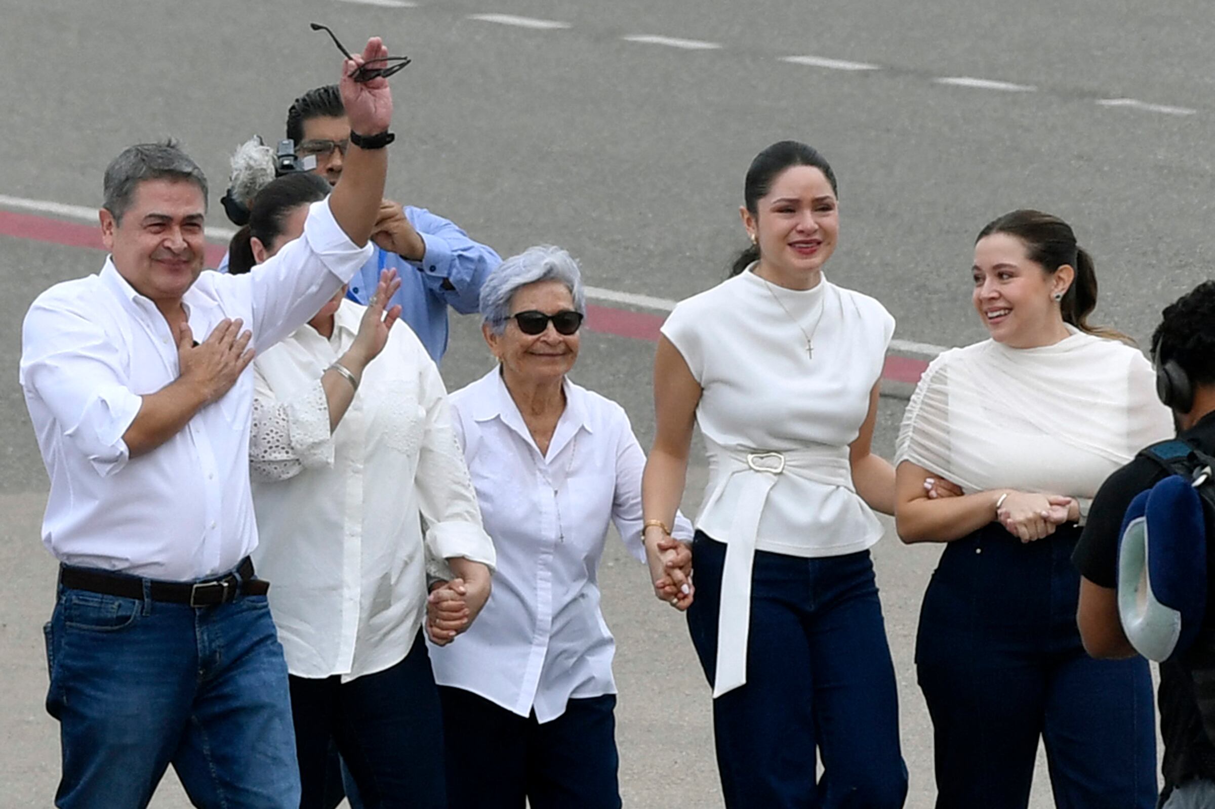 El expresidente de Honduras (2014-2022), Juan Orlando Hernández (izquierda), saluda junto a (de izquierda a derecha) su esposa Ana García, su madre Elvira Alvarado y sus hijas Isabela y Daniela tras su llegada en un vuelo privado al Aeropuerto Internacional de Palmerola, en Comayagua, a 80 km al norte de Tegucigalpa, el 26 de julio de 2026. Hernández regresa a Honduras para enfrentar cargos de corrupción tras haber sido indultado el año pasado por el presidente estadounidense Donald Trump, luego de una condena de 45 años por narcotráfico, antes de las elecciones presidenciales ganadas por su compañero conservador Nasry Asfura. (Foto de Orlando SIERRA / AFP)