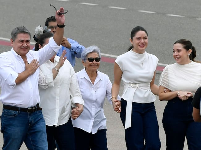 El expresidente de Honduras (2014-2022), Juan Orlando Hernández (izquierda), saluda junto a (de izquierda a derecha) su esposa Ana García, su madre Elvira Alvarado y sus hijas Isabela y Daniela tras su llegada en un vuelo privado al Aeropuerto Internacional de Palmerola, en Comayagua, a 80 km al norte de Tegucigalpa, el 26 de julio de 2026. Hernández regresa a Honduras para enfrentar cargos de corrupción tras haber sido indultado el año pasado por el presidente estadounidense Donald Trump, luego de una condena de 45 años por narcotráfico, antes de las elecciones presidenciales ganadas por su compañero conservador Nasry Asfura. (Foto de Orlando SIERRA / AFP)