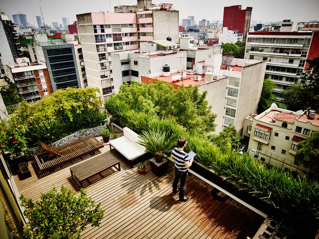 Man standing with digital tablet on rooftop garden terrace of home looking out at city skyline