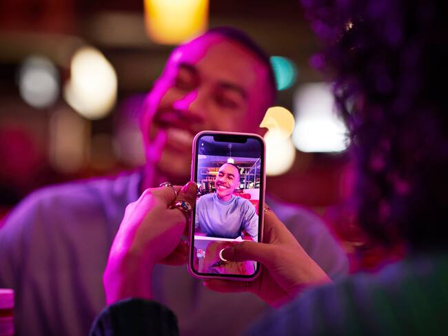 Mujer tomándole foto a su pareja sonriendo con el celular (Getty Images)