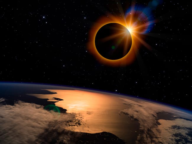 Eclipse solar con halo naranja sobre el planeta Tierra, en el oscuro cielo estrellado. Foto: Getty Images.