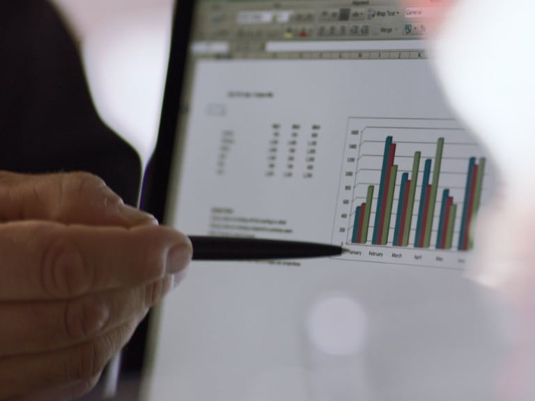 Asesor financiero muestra resultados de gráfico de barras en computadora portátil (Getty Images)