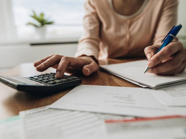 Mujer utilizando una calculadora mientras anota diferentes datos en un cuaderno / Foto: GettyImages