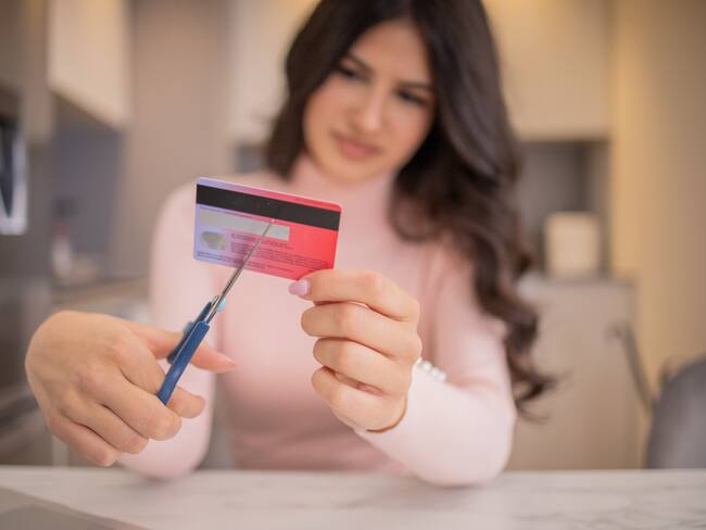 Mujer cortando el flástico de una tarjeta débito. (Foto vía Getty Images)
