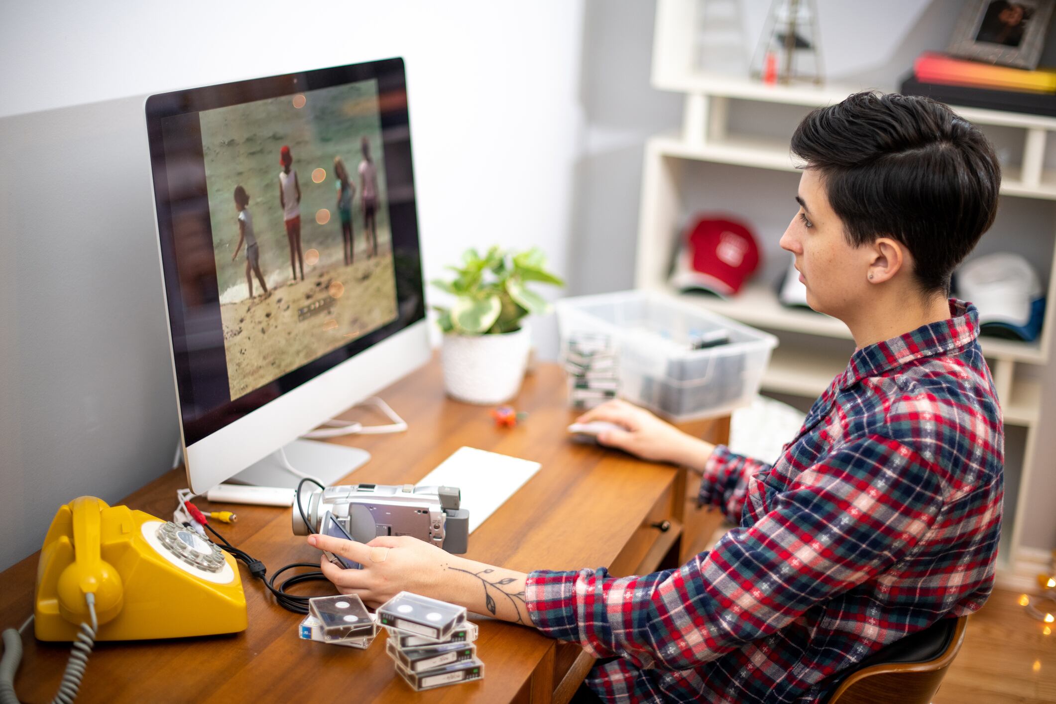Woman edits home movies in her home office during the coronavirus pandemic. She looks at the footage playing on the computer screen as she edits.