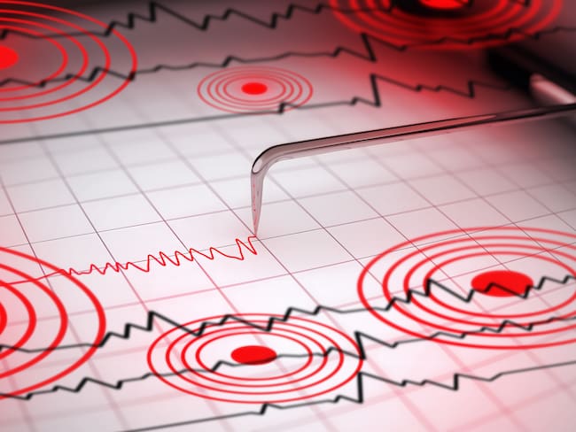 Close-up of a seismograph machine needle tracing seismic waves, indicative of earthquake activity, on graph paper with epicenter rings.