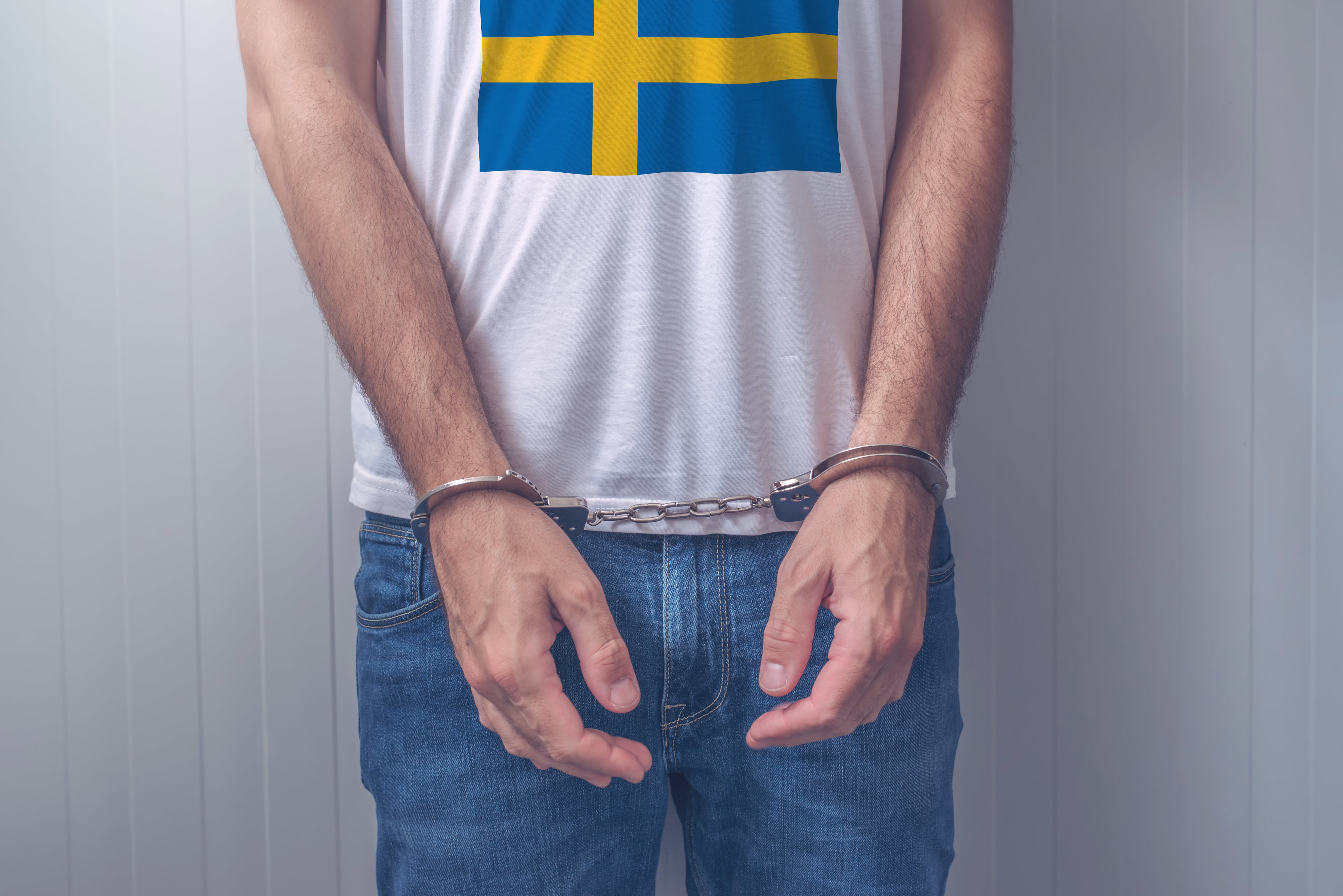 Arrested man with cuffed hands wearing shirt with Swedish flag. Unrecognizable male person in jeans with handcuffs held in police station for being suspected of a crime. GETTY IMAGES.