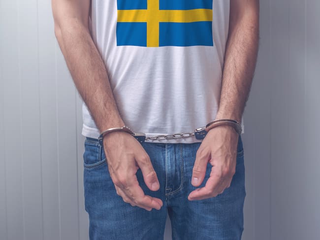 Arrested man with cuffed hands wearing shirt with Swedish flag. Unrecognizable male person in jeans with handcuffs held in police station for being suspected of a crime. GETTY IMAGES.